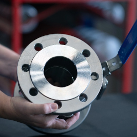 Two hands are prominently displayed in the foreground, firmly holding a large gasket, symbolizing precision and strength. In the blurred background, an industrial area unfolds, marked by machinery and the structured chaos of a manufacturing environment.