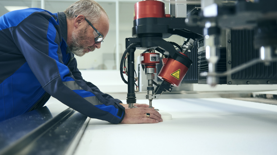 A middle-aged man is concentrated on his work in a factory setting, actively engaged in engineering a product with the assistance of an innovative machine. He is dressed in work attire, which includes protective glasses, emphasizing the importance of safety in this environment. The image conveys a sense of expertise and dedication, as the man applies his skills to operate the machinery, showcasing the blend of human craftsmanship and modern technology in manufacturing.